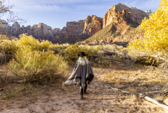 USA, Utah, Zion National Park, Rear view of woman in poncho and hat walking near Virgin River