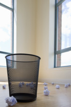 Crumpled waste paper on floor around empty bin