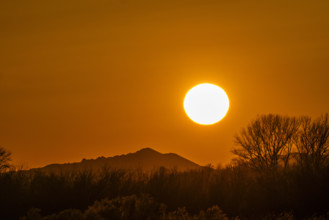 Sun setting above hills against orange sky. Bellevue, Idaho, USA.