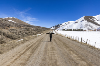 Rear view of woman on empty dirt road in snowy landscape. Bellevue, Idaho, USA.