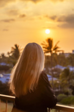 Rear view of blonde woman viewing sunset from deck. Kona, Hawaii, USA.