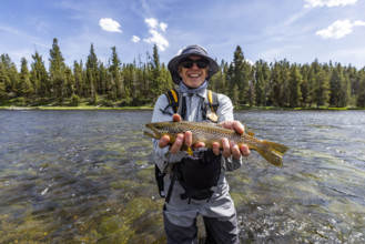 Portrait of smiling fly fisherman holding trout before releasing. , Wyoming, USA.