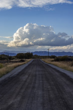 White puffy clouds over empty rural road and mountains. Bellevue, Idaho, USA.