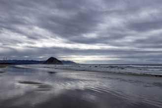 Storm clouds above beach with Morro Rock in distance, Morro Bay, California, USA.