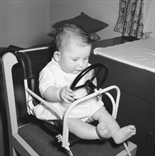 Baby at the wheel. Tubby Block's baby in a play chair with steering wheel. Kenya, 30 August 1954.