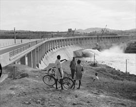 At the newly completed Owen Falls Dam. People with bicycles chat at the site of the brand new Owen