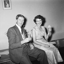 Cheers. Cheerful couple shown seated with drinks below a picture of Queen Elizabeth II at an RAF