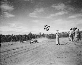 Waving the chequered flag. A man waves a chequered flag as a Lancia racing car crosses the