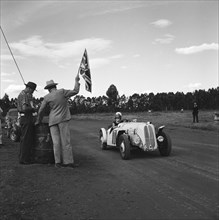 On your marks. A man holds up a union jack flag for car number 101, an Anglia Special, at the start