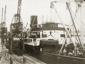 Unloading a locomotive tender from SS Harmonides. Cranes onboard the SS Harmonides hoist a
