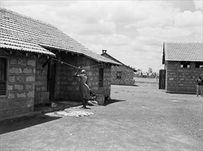 African housing. Two woman chat outside the doorway to one of three houses with pitched, tiled