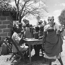 Interview board. A queue of women at a cleansing ceremony wait near a desk manned by two men