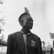 Witch doctor. Upper body shot of a witch doctor wearing a jacket and a feathered hat. Kenya, 20-28