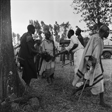 Cleansing ceremony. Two men brush bundles of branches against a woman wearing jewellery as she