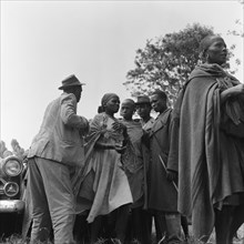 Group at a cleansing ceremony. Three men with hats and batons stand either side of a queue of women