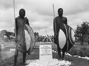 Maasai beside a coronation plaque. Maasai warriors stand either side of a memorial plaque