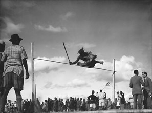 High jump. A man holding a baton attempts the high jump at a 'ngoma', a word meaning drum that is