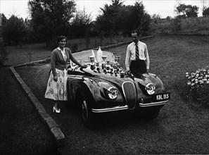Manussis with trophies. Racing driver John Manussis poses with a woman next to a Jaguar Coupe