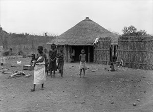 Mozambique natives. A group of children outside a wooden hut with a thatched roof. A barefooted