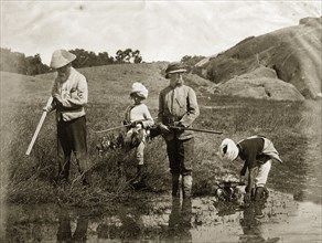 Snipe hunting. Two British snipe hunters stand, shotguns in hand, as their young Indian assistants