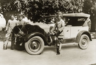 Brown bears on a Cadillac. An Indian gentleman in Western dress poses, shotgun in hand, after a