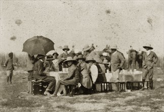 Hunting party lunch. A hunting party comprised of British men and women seek shade under solatopi