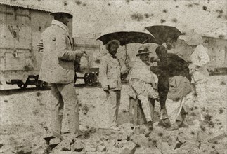 A shave in the shade. A British gentlemen is shaded with parasols as he is shaved by an Indian