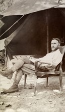 European camper. A European man relaxing in a chair outside his tent, looks up from the letter he