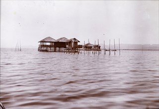 Lake dwellings in Burma (Myanmar). Two wooden dwellings on stilts project from the calm waters of a