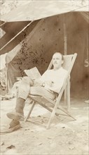 Relaxing in camp. A European man reads a book whilst reclining in a deckchair under the canopy of a