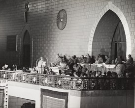 Addressing the sixth Buddhist Synod. One of several Buddhist monks, seated on a raised balcony,