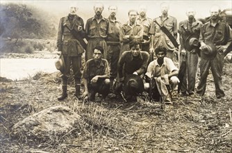 A trekking party in the jungle. Eight European men pose for a group portrait beside a river with