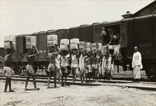 Queuing up to load a freight train. A team of workers carry boxes on their heads and form a queue,