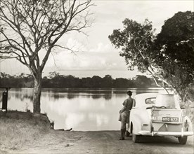 Man gazing over picturesque lake. A solitary man leans against a loaded car parked by the side of a