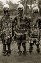 Juju practitioners. Three juju dancers in costume wear wooden masks on top of their heads, ornate
