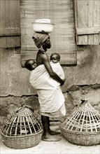 Yoruba woman with 'pickins'. A barefooted Yoruba woman wearing a headscarf carries two babies