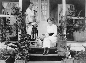 Pets and plants at number 61. Two women on the veranda of a timber-framed colonial bungalow, number