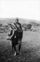 Kamba boy. Informal portrait of a smiling Kamba boy wearing a striped blanket. Kenya, circa 1927.