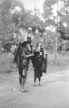 Kamba women with children. Two barefooted Kamba women in traditional dress carry small children on