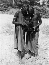 Looking through the viewfinder. Two African men, possibly Maasai, peer into the viewfinder of a