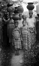 Carrying pots. Several Nigerian women and a young girl wear wraparound blankets and balance large