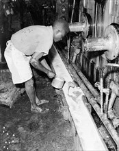 Testing juice at a sugar mill. An African worker dips a testing pot into a trough of juice being