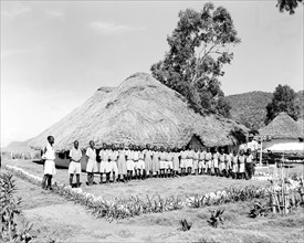 Miwani Sugar Mills school. A row of students in school uniform pose outside a thatched school hut