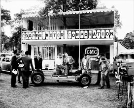 Cooper Motor Corporation. A group of European men chat beside the bare chassis of a car at the