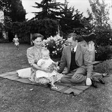 In the Russel's garden. A couple sitting on a rug in the Russel family's garden entertain a baby