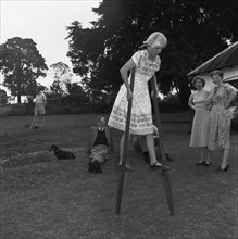 Miss Russel walks on stilts. The Russel's daughter attempts to walk on wooden stilts in the family