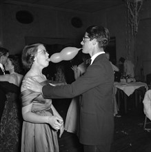 Balloon antics. A formally dressed couple clown around with a balloon at a dance held for the