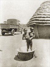 Child and baby in bath tub. A semi-naked child stands inside an empty bath tub, holding a baby on