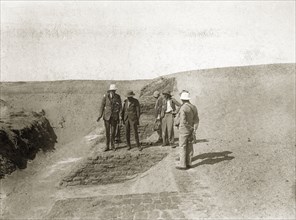 Archaeological excavation. European men with cameras or recording equipment walk along an exposed