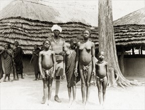 Saleh and Balanda girls. An African man wearing a turban with shorts and long socks stands outside